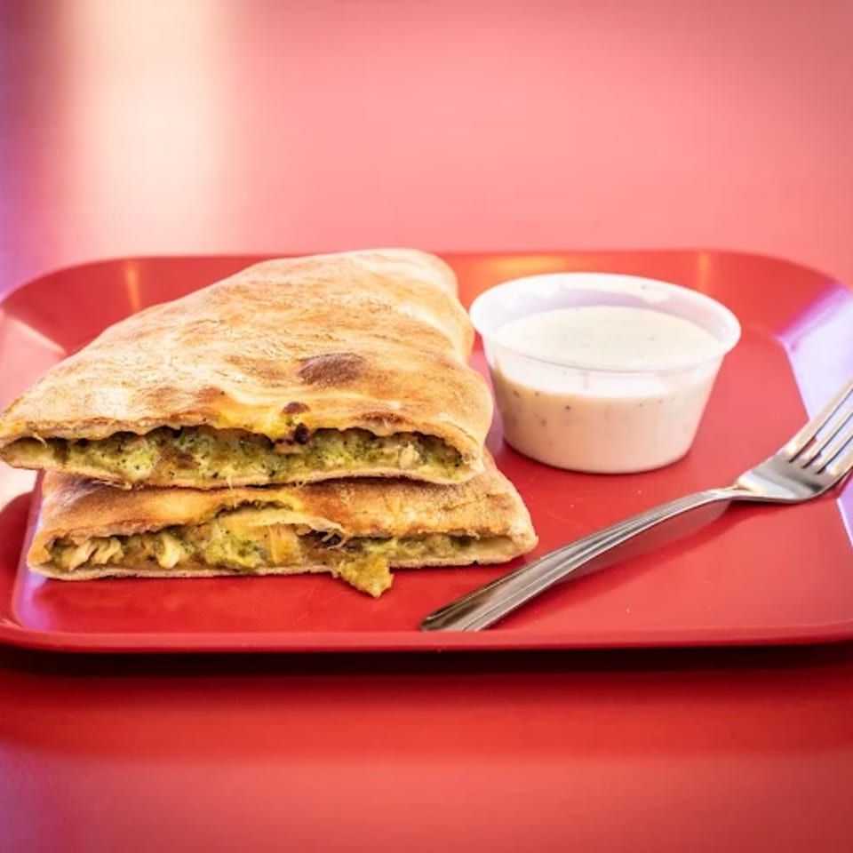 Two pesto chicken calzones with a side of ranch dressing and a fork on a red plate.