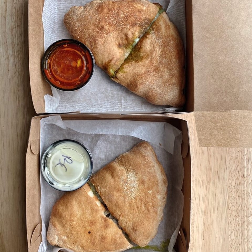 Two calzones from The Dough Co. in takeout boxes with dipping sauces.