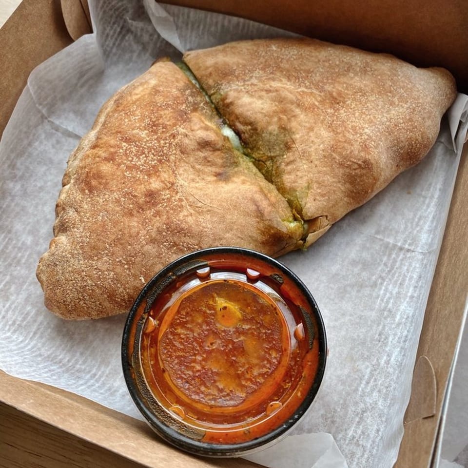 A calzone from The Dough Co. with a side of marinara sauce in a takeout box.
